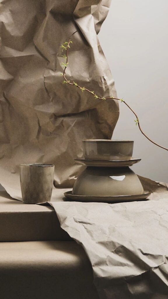 Minimalistische productfotografie van keramieken servies en bekers met crinkled papier en een natuurlijke tak, rustige aardetinten voor duurzame merken